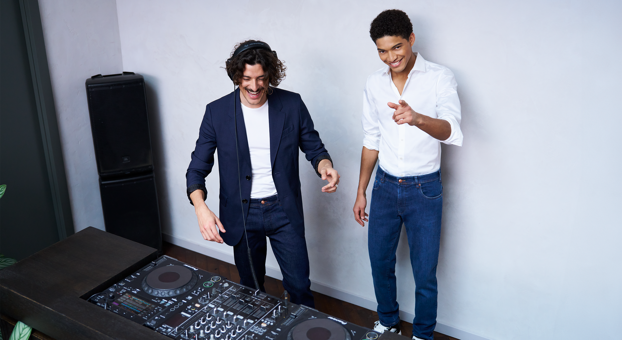 Two men standing next to a DJ turntable in a room with a white wall.